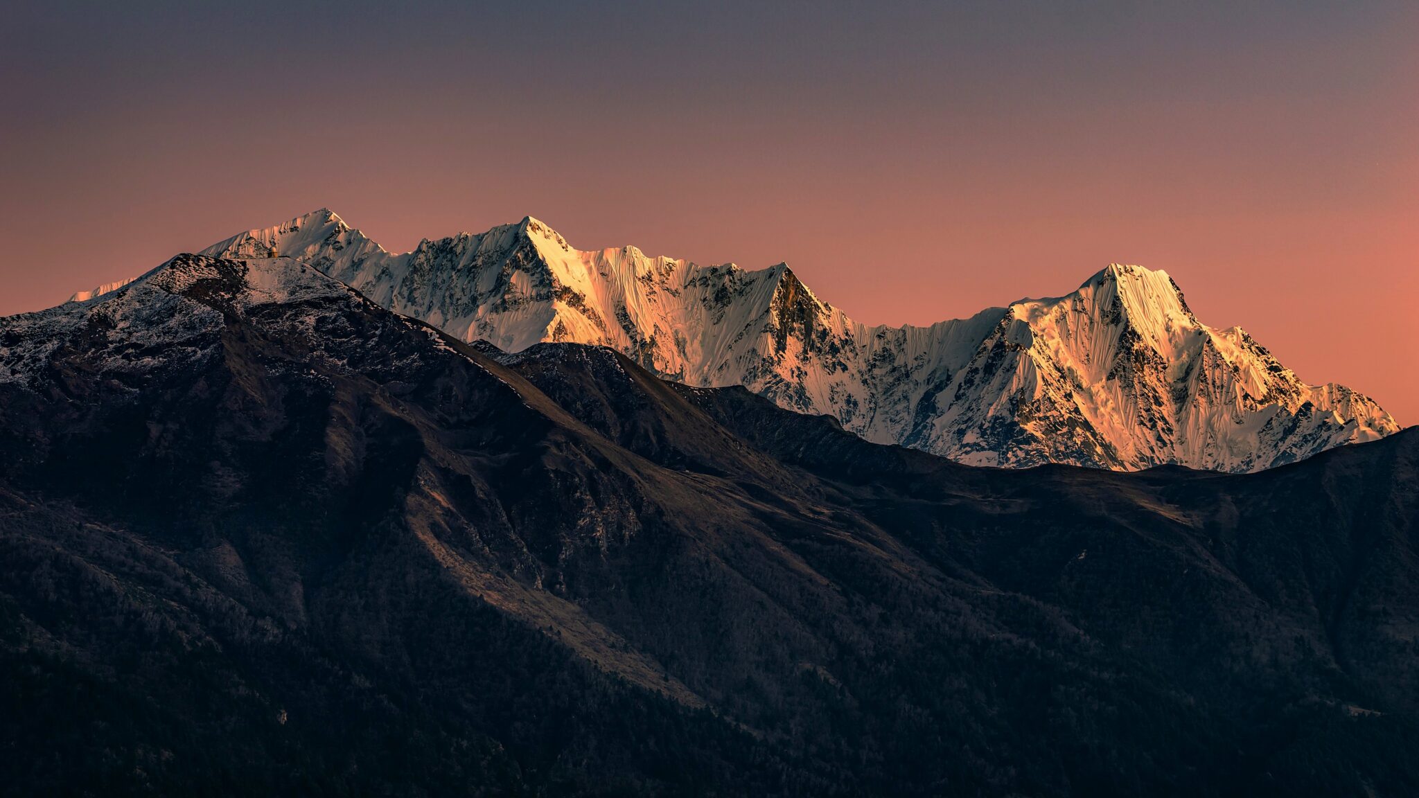 Snow-covered Himalayan peaks glowing in the last light under a dusk sky, dark foothills below