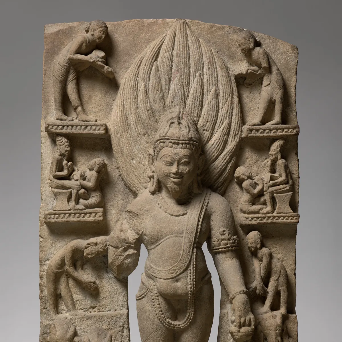 A sandstone stele of Agni standing before a tall halo of flames, crowned, with small figures of Brahmins at the fire sacrifice in the panels on either side