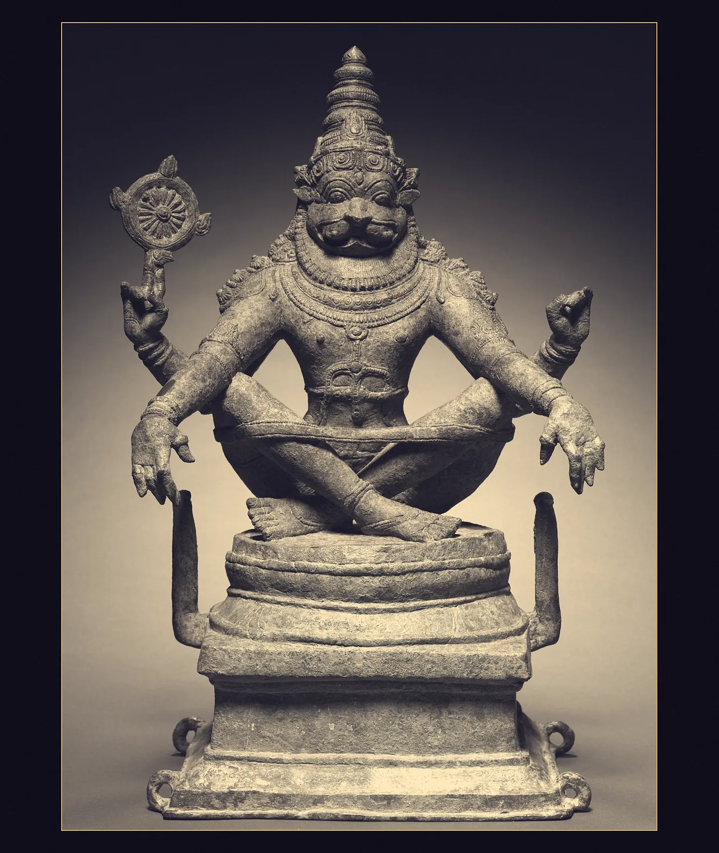 A Chola bronze of the lion-headed Narasimha seated cross-legged, the discus raised in his upper right hand